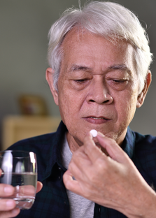 Anciano a punto de tomar una pastilla con un vaso de agua