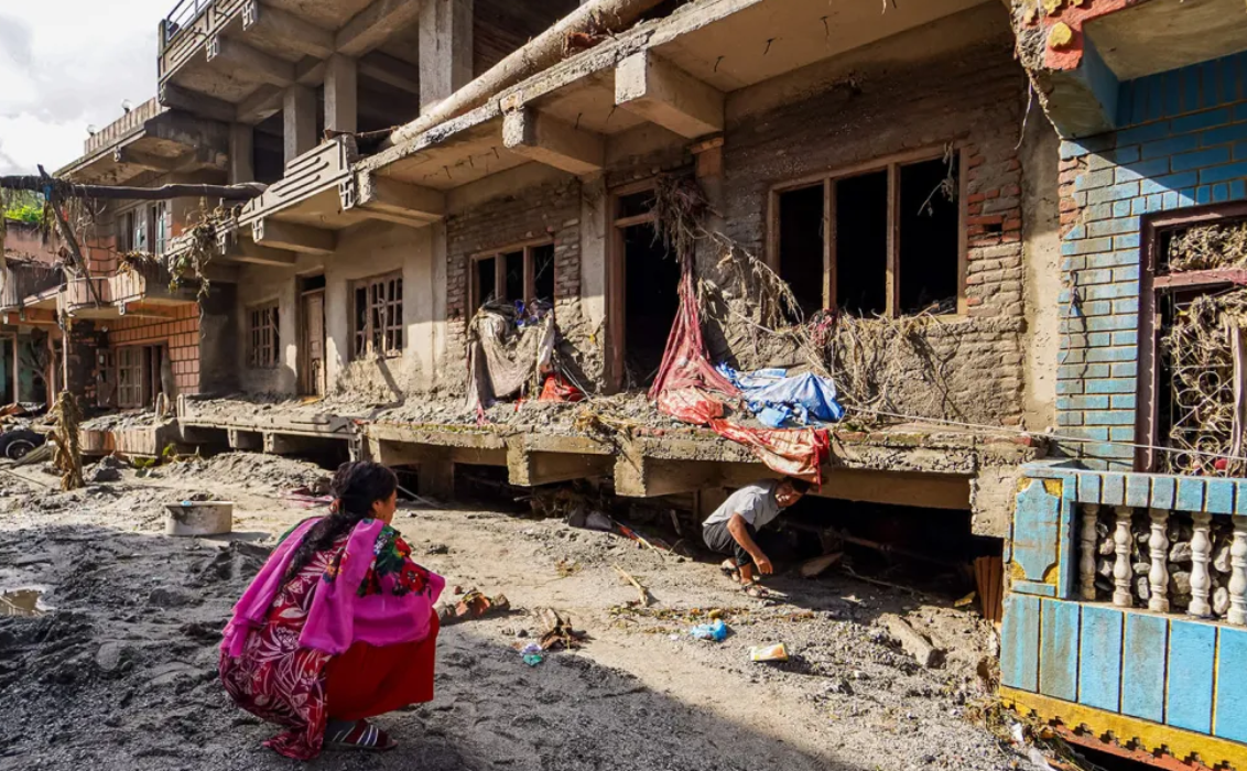 Two people inspect mud- and debris-covered homes after severe flooding in Nepal in 2026.