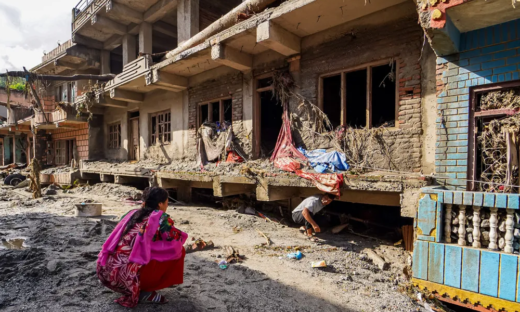 Two people inspect mud- and debris-covered homes after severe flooding in Nepal in 2026.